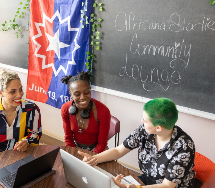 A professor sits and talks with two students in the Africana Studies community lounge