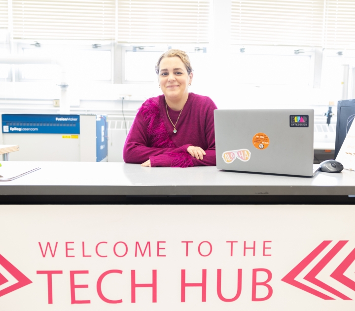 Jaclyn Ellis sits behind a desk with a sign that says welcome to the tech hub